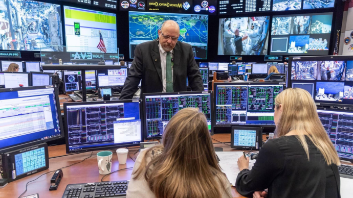 Royce Renfrew instructs people working at computers in the NASA Mission Control Center
